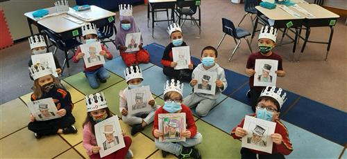 Photo of students sitting on a carpet holding up a coloring page of Duke Ellington.